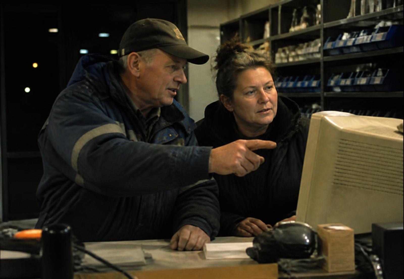 Two dealership employees at a parts counter at night looking at an aging computer terminal